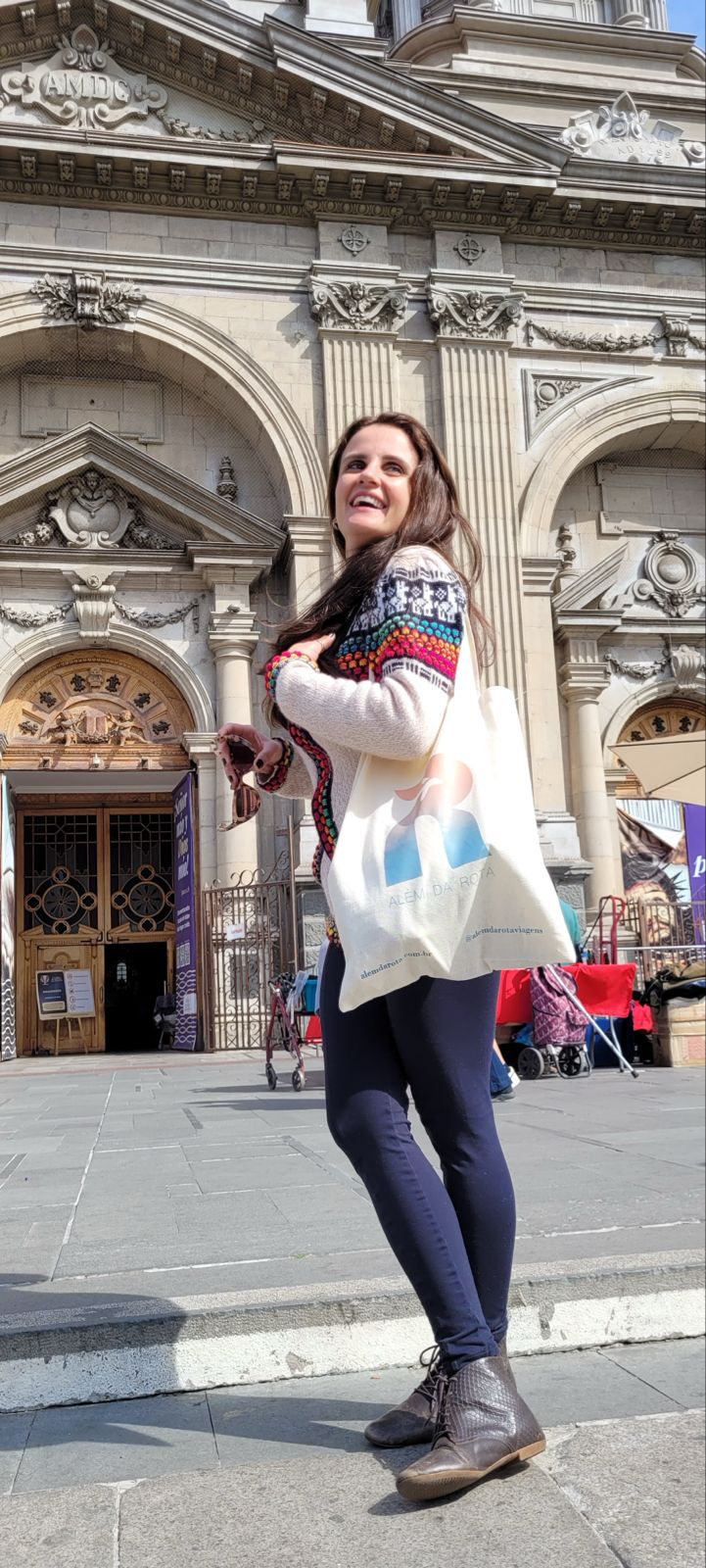 Mariana com a ecobag da Além da Rota em frente a uma igreja histórica